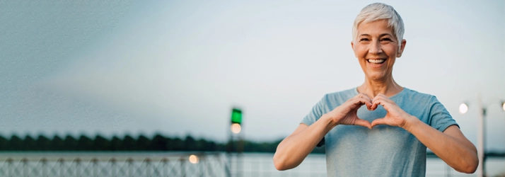 A woman outdoors forming a heart shape with her hands.