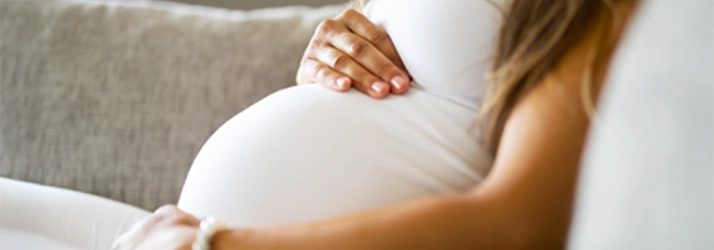 A pregnant woman sitting on a couch, gently holding her belly.